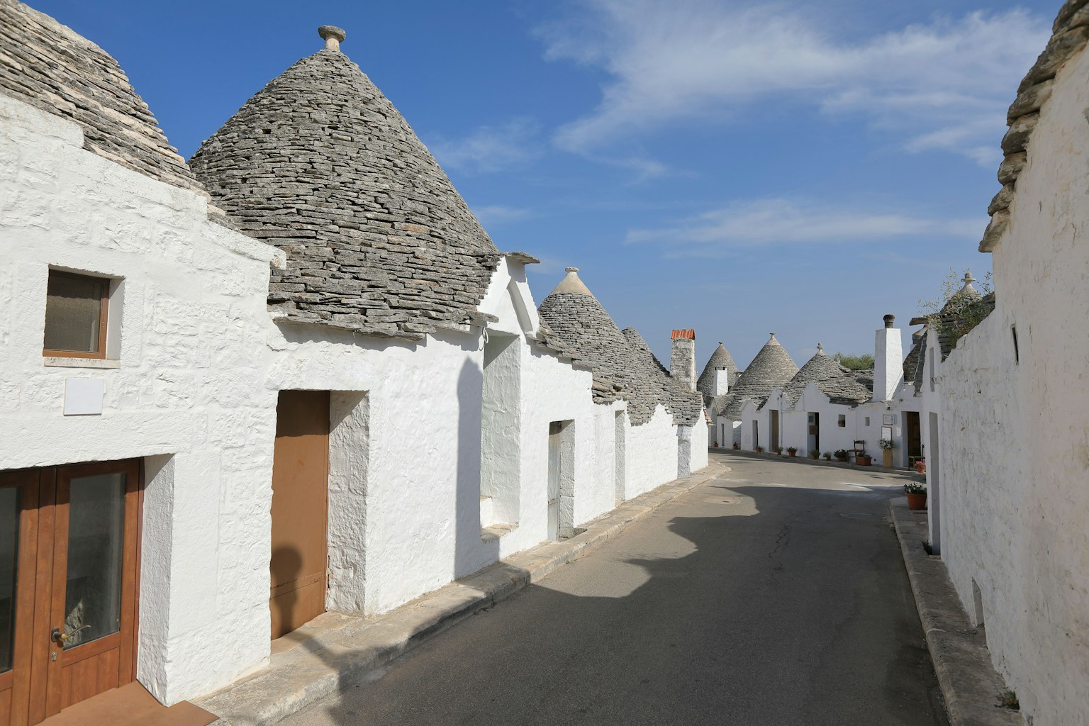 Quiet street lined with white trulli houses featuring gray stone roofs