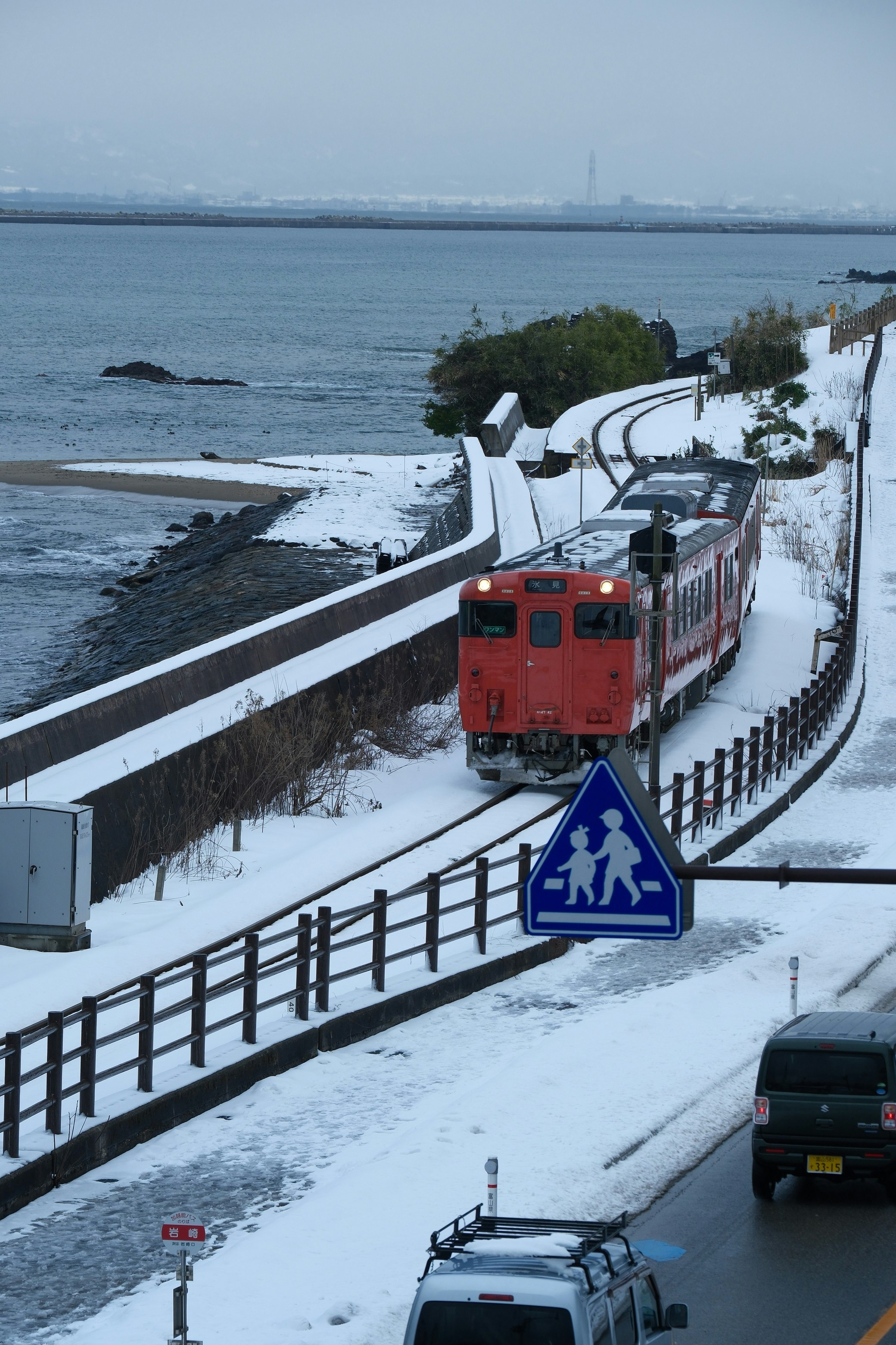 雪の海岸沿いを走る氷見線の列車