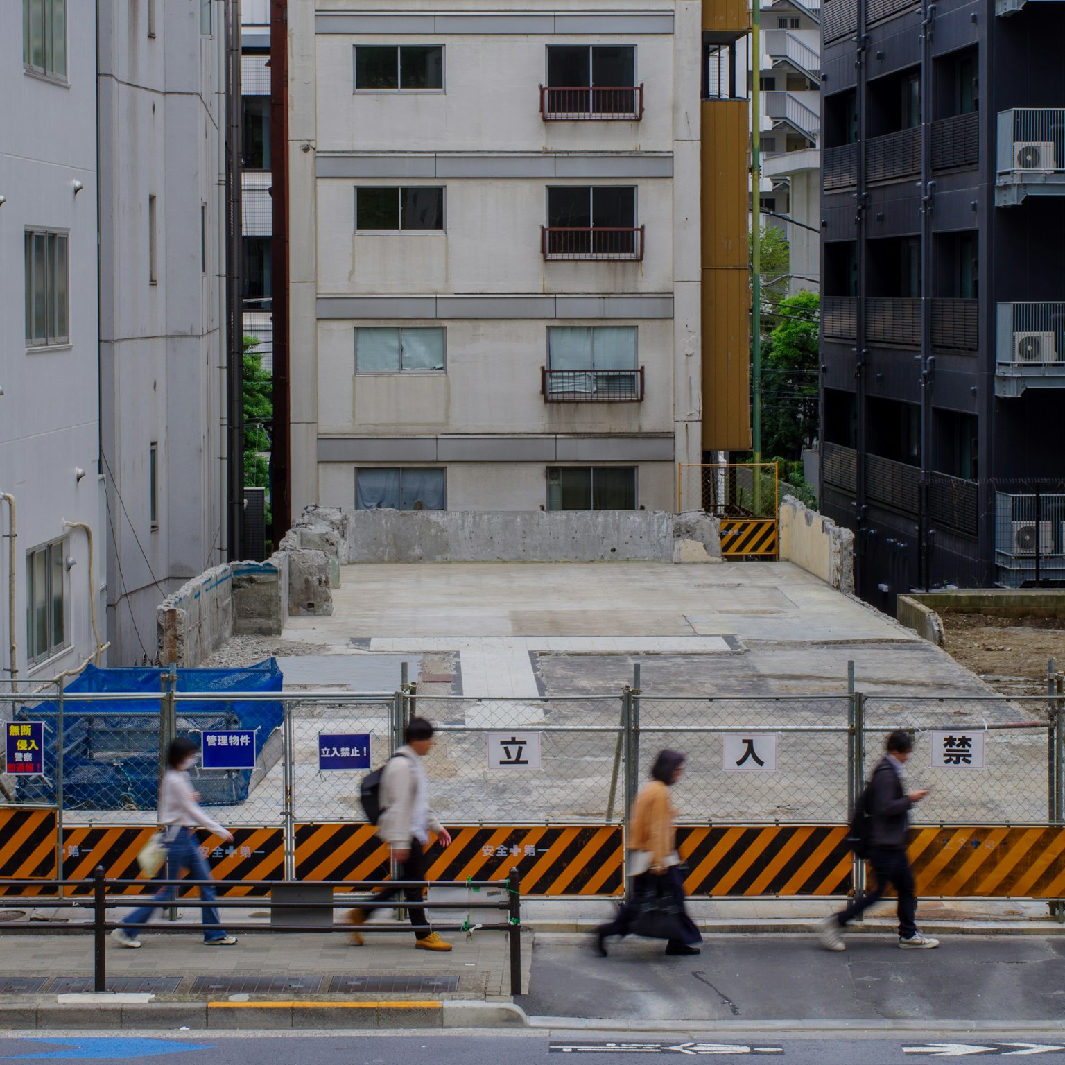 Personas caminando frente a un sitio de construcción con edificios circundantes