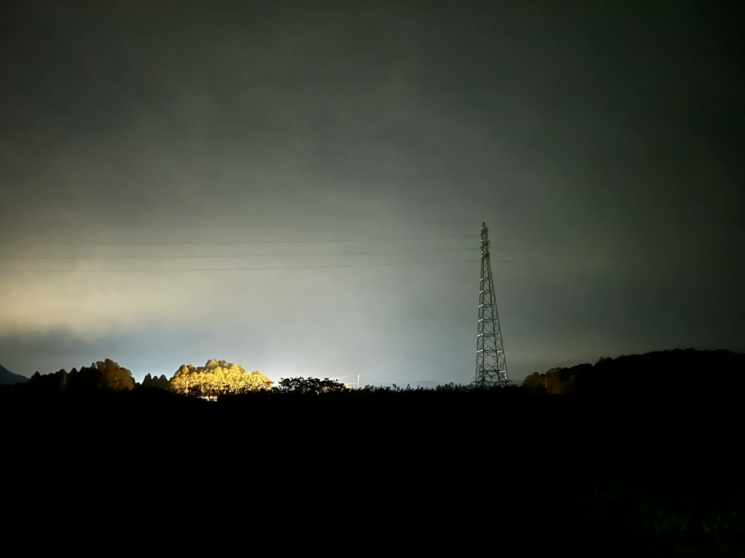 Radioturm vor einem dunklen Himmel mit fernem Licht silhouettiert