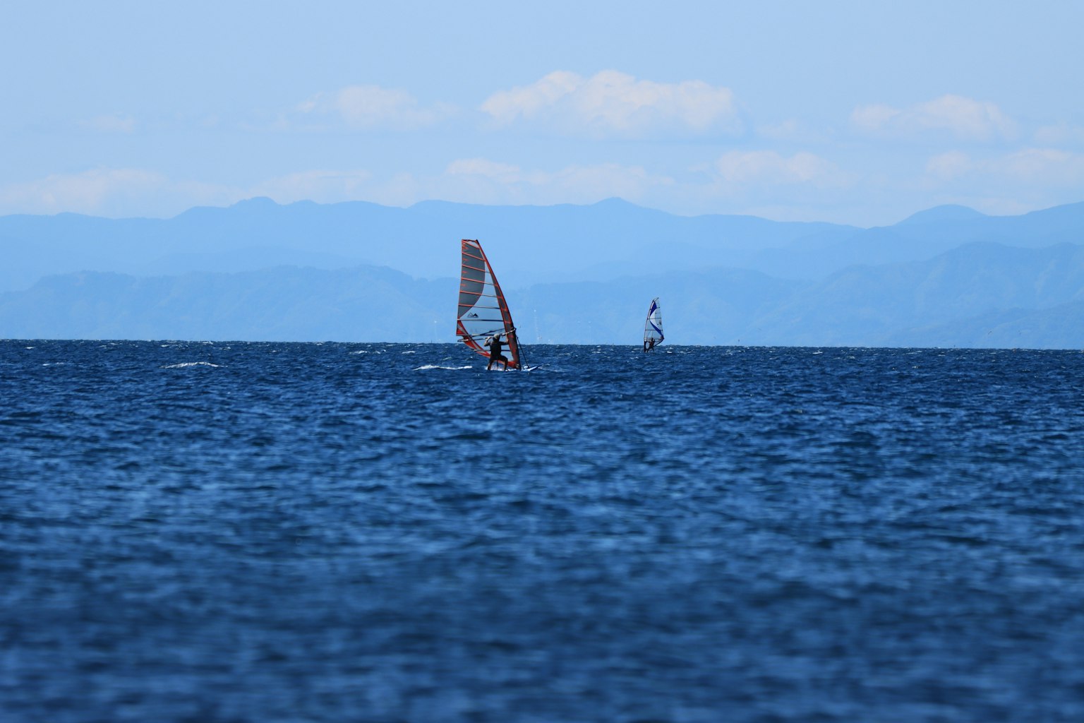 Sailboats on a blue ocean with distant mountains