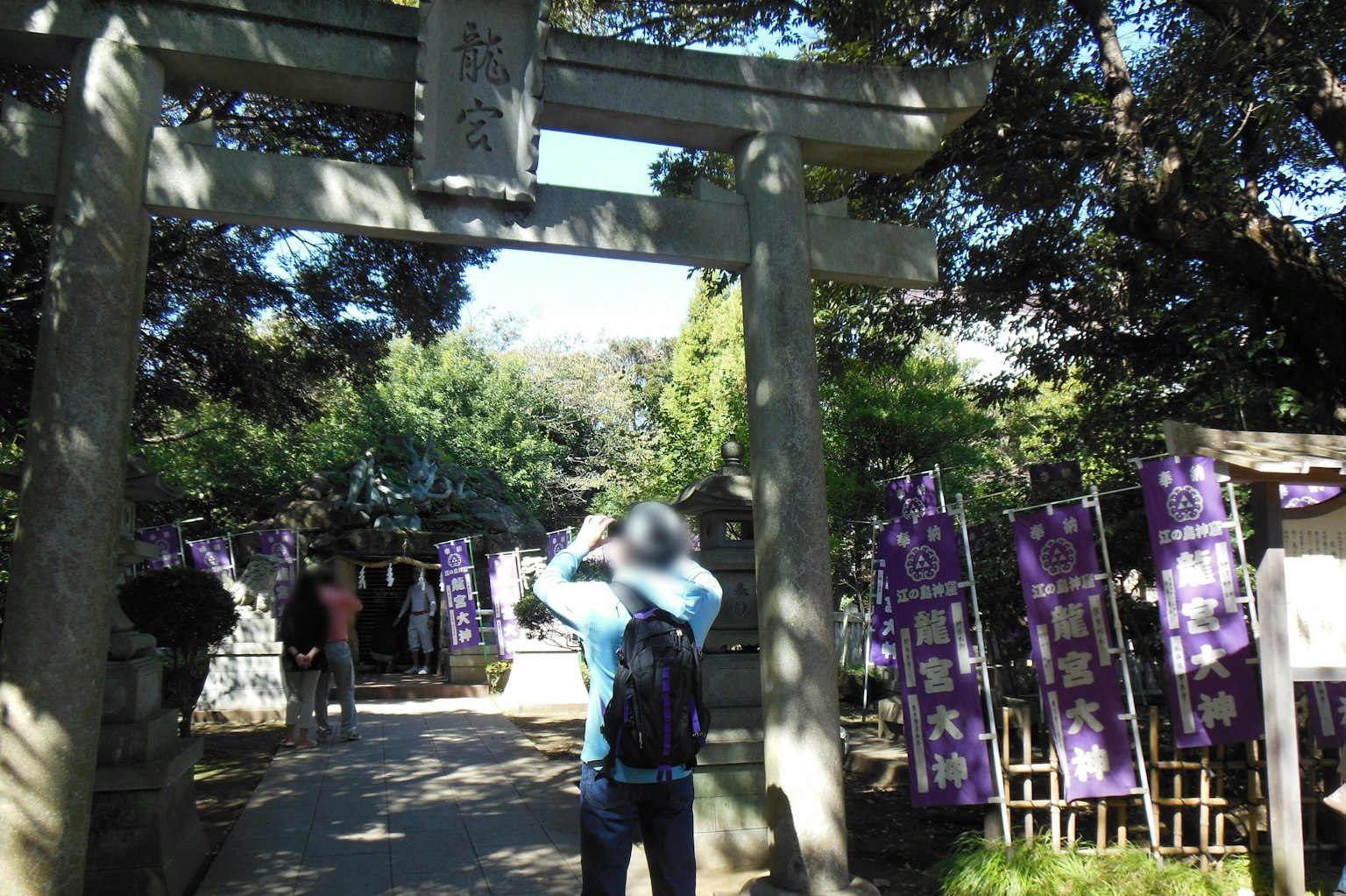 Cảnh đền thờ với cổng torii và du khách với băng rôn màu tím