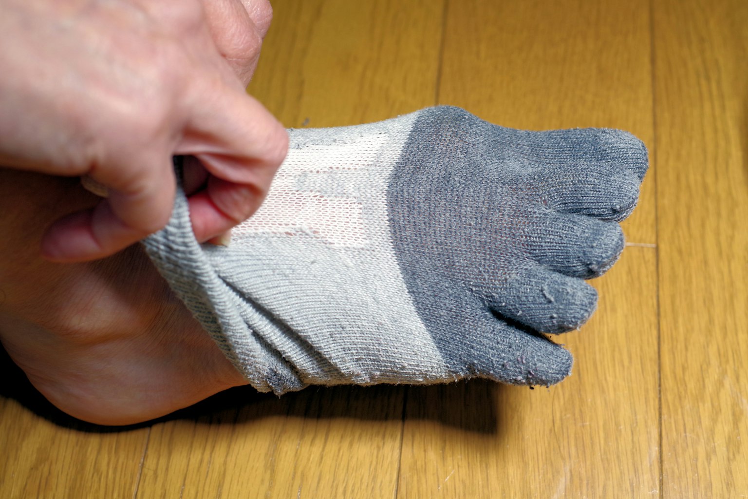 Une main en train de mettre une chaussette à orteils grise et blanche sur un pied