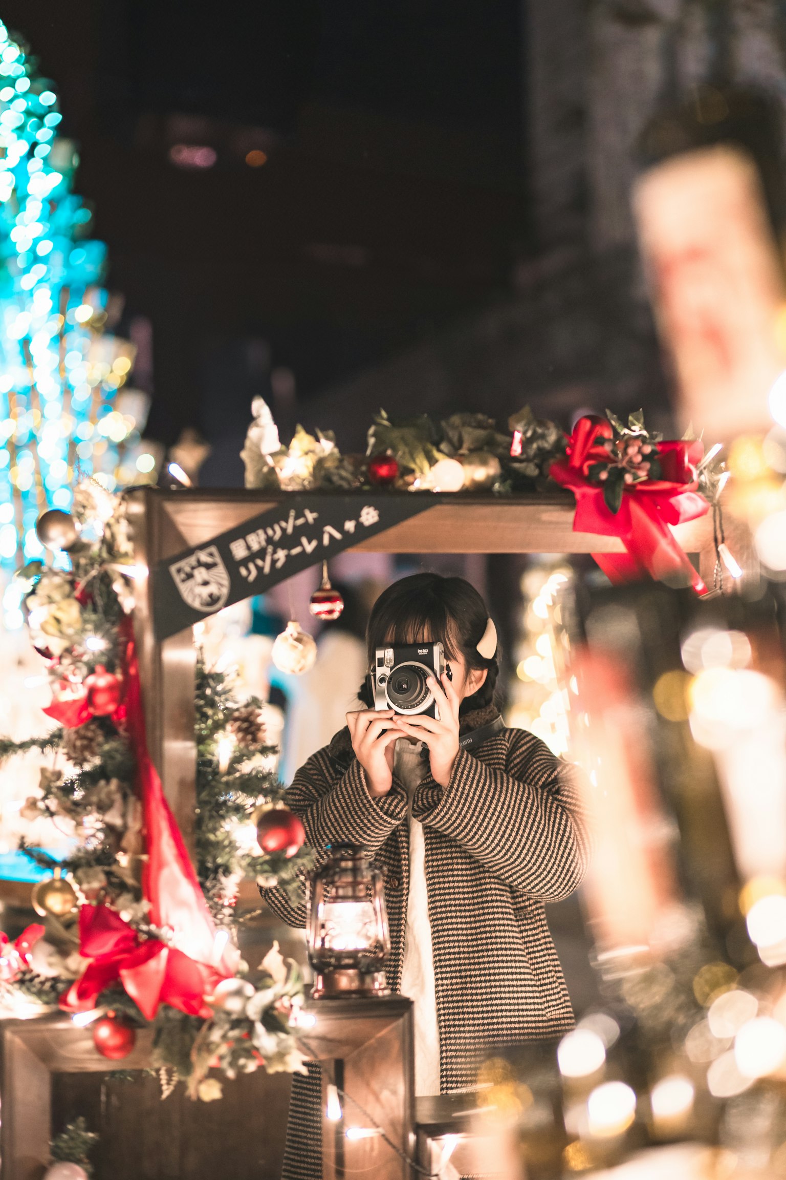 Wanita memegang kamera dalam suasana malam yang didekorasi Natal