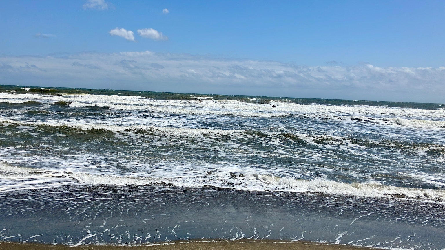 Wellen brechen am Ufer unter einem blauen Himmel