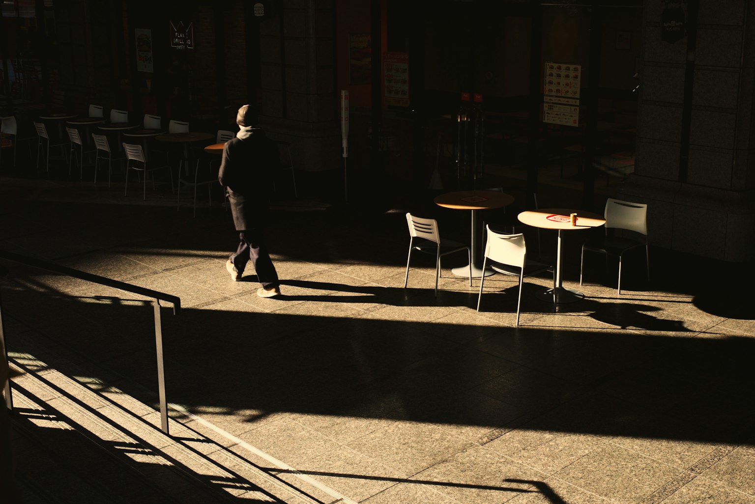 Una silhouette di una persona che cammina in un'area caffè poco illuminata con tavoli