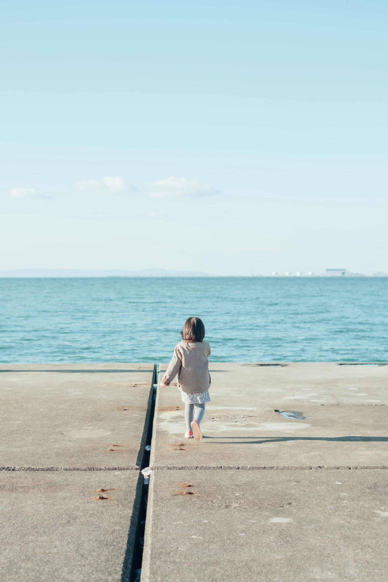 Enfant marchant vers la mer sur un quai en béton