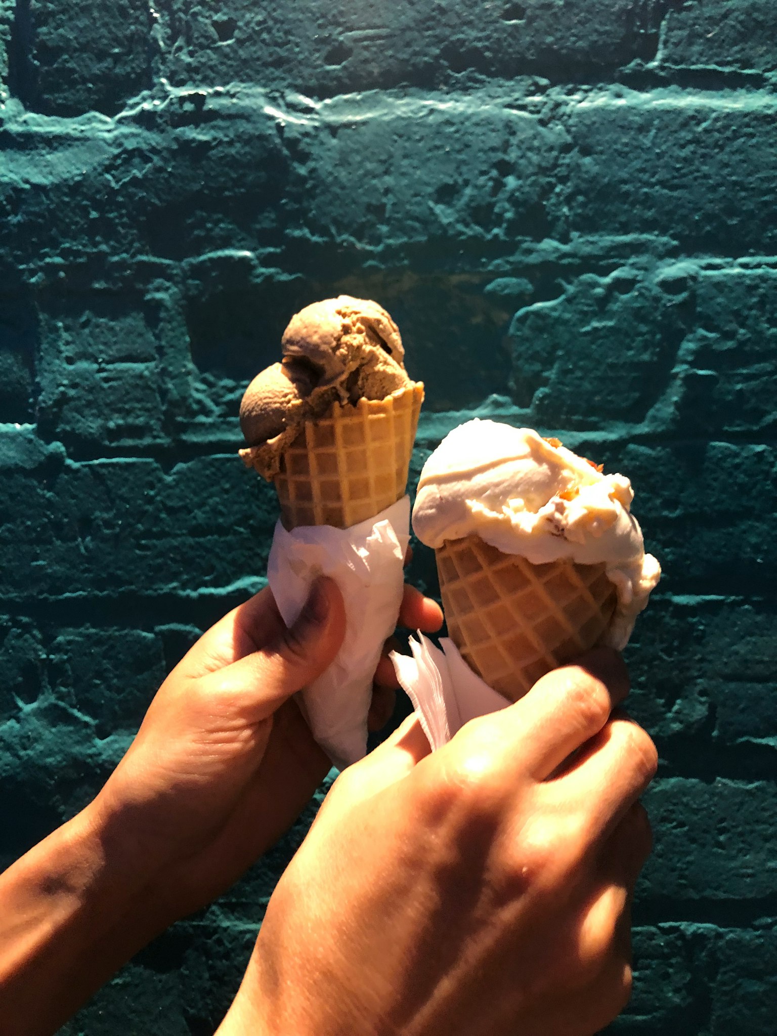 Two ice cream cones held in hands with different flavors