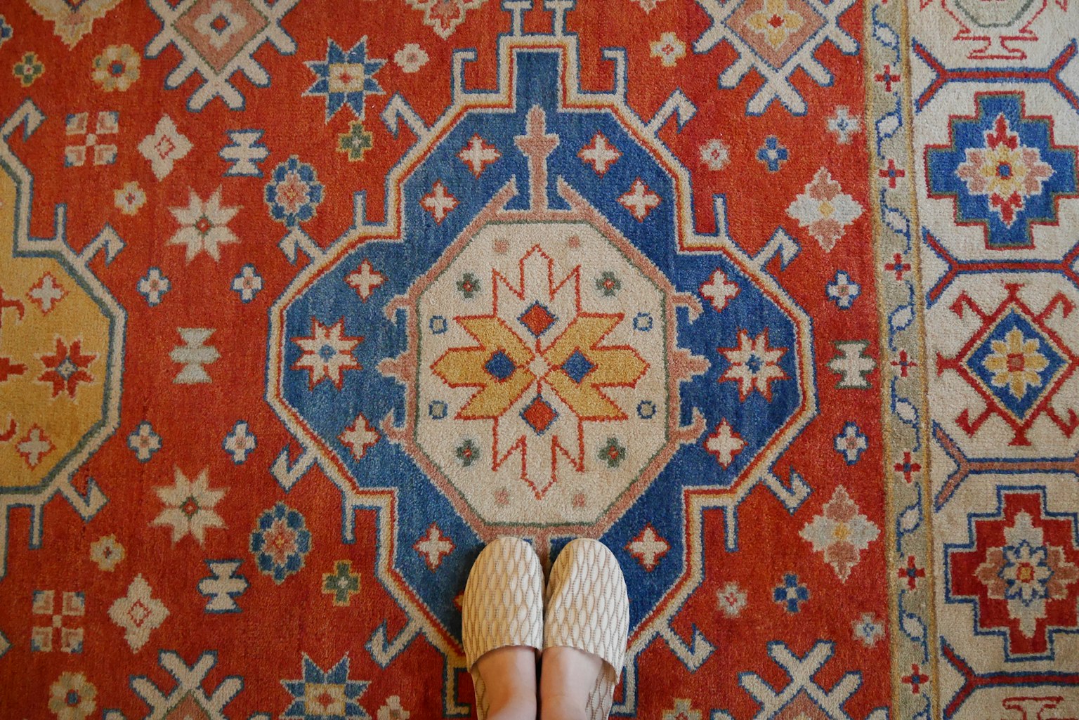Pies en zapatos blancos sobre una alfombra roja con patrones