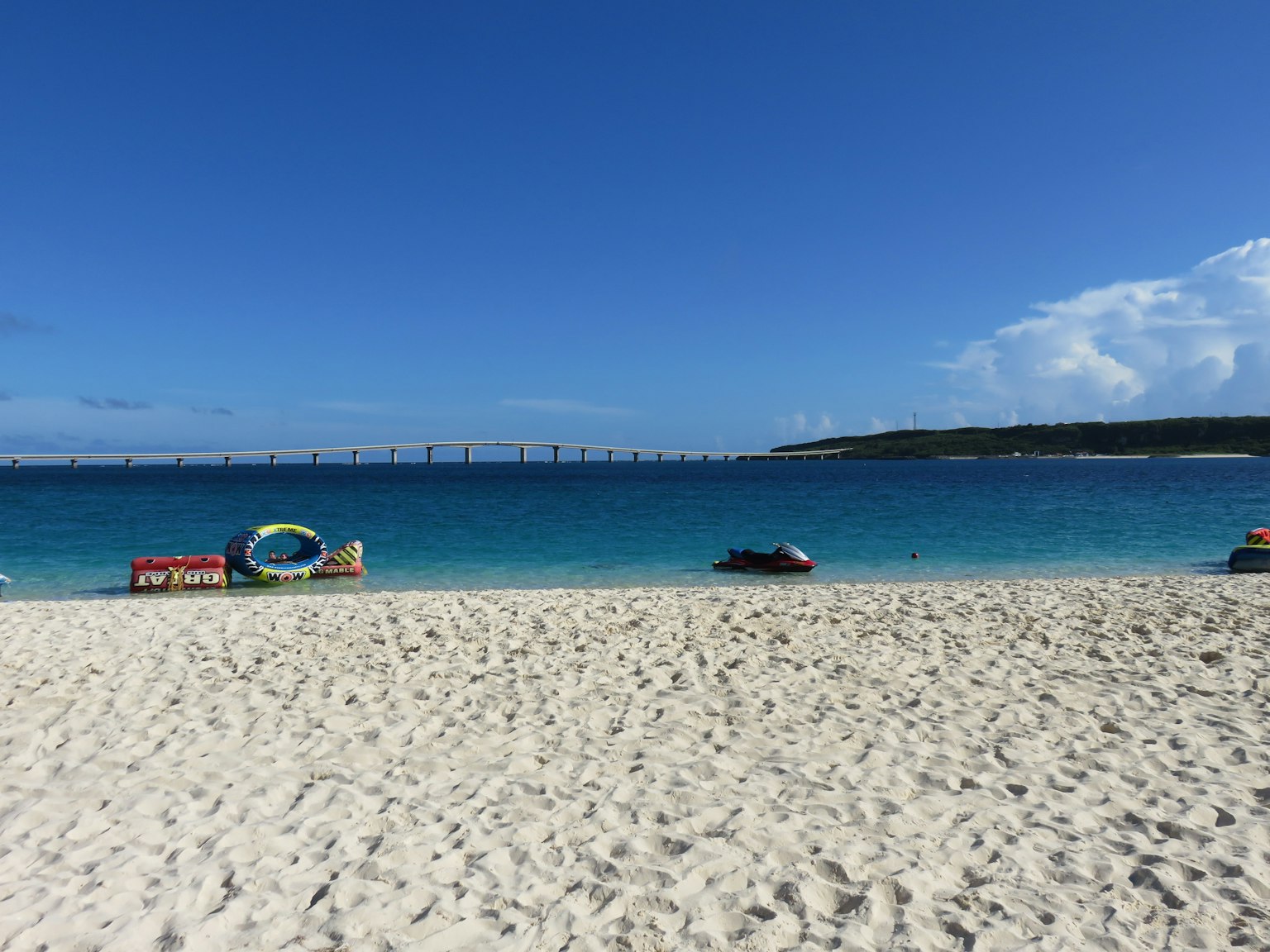 Scenic beach view with blue sky and sandy shore bridge visible in the distance