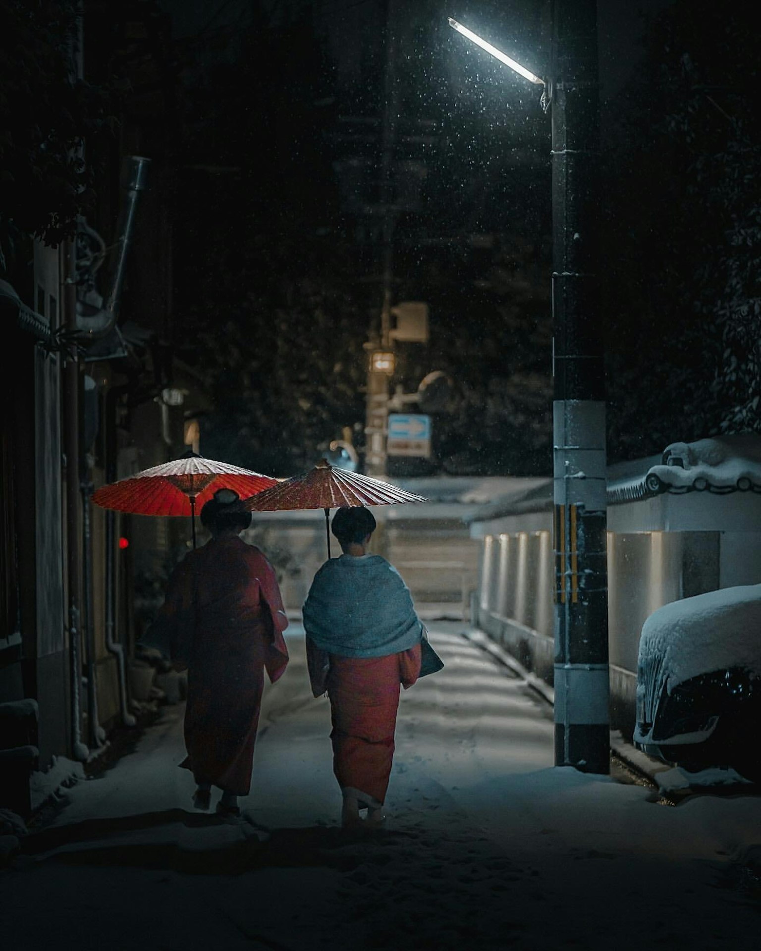Zwei Frauen gehen nachts in einer schneebedeckten Gasse mit einem roten Regenschirm