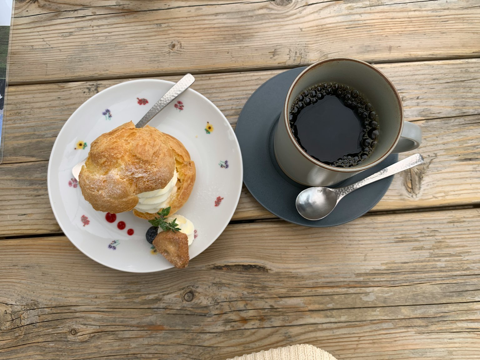 Scone hojaldrado cubierto con crema en un plato junto a una taza de café sobre una mesa de madera