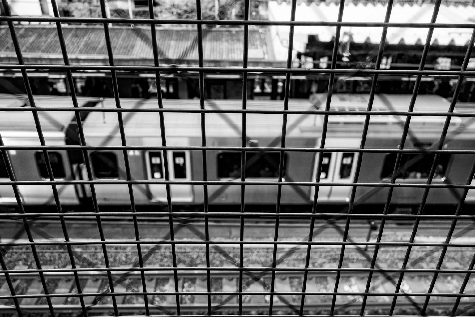 Primer plano de un tren en una estación de ferrocarril enmarcado por una estructura de rejilla