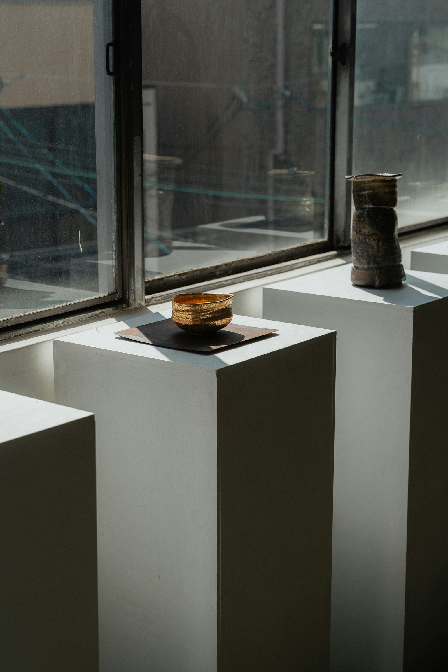 Piring dan vas di atas dudukan putih dekat jendela