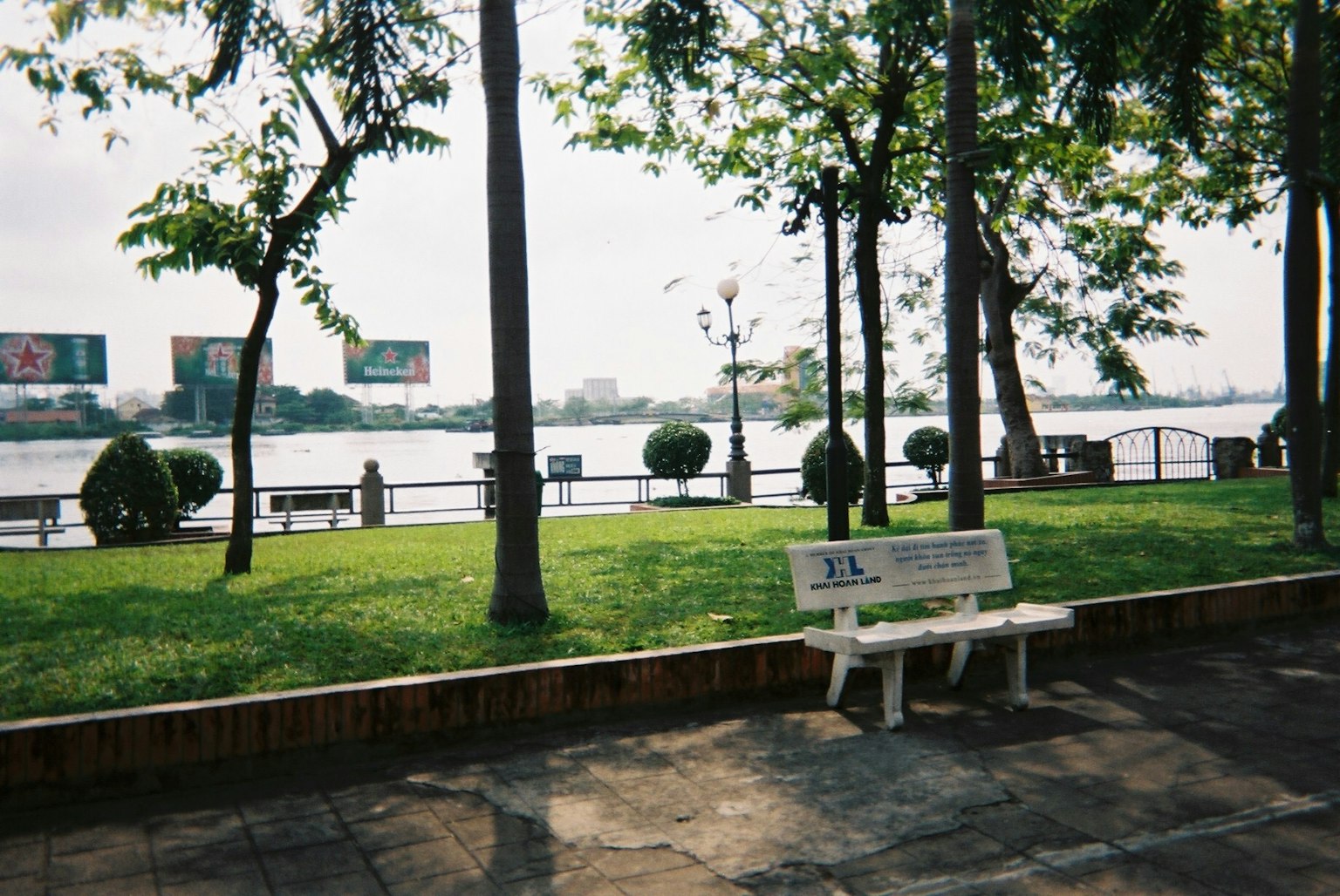 Eine weiße Bank in einem Park am Fluss mit grünem Gras und Bäumen