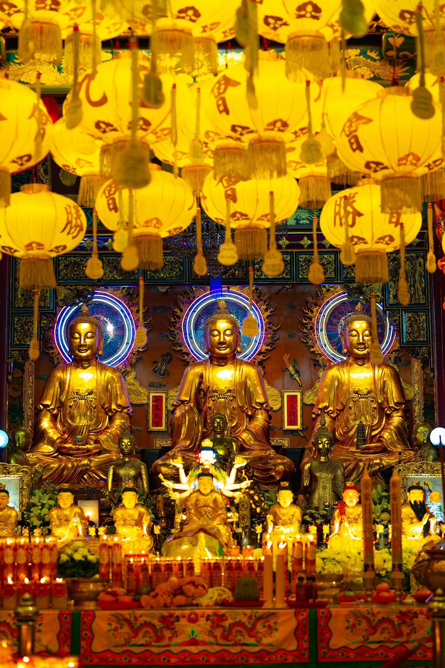 Interno di un tempio con statue di Buddha dorate e lanterne gialle