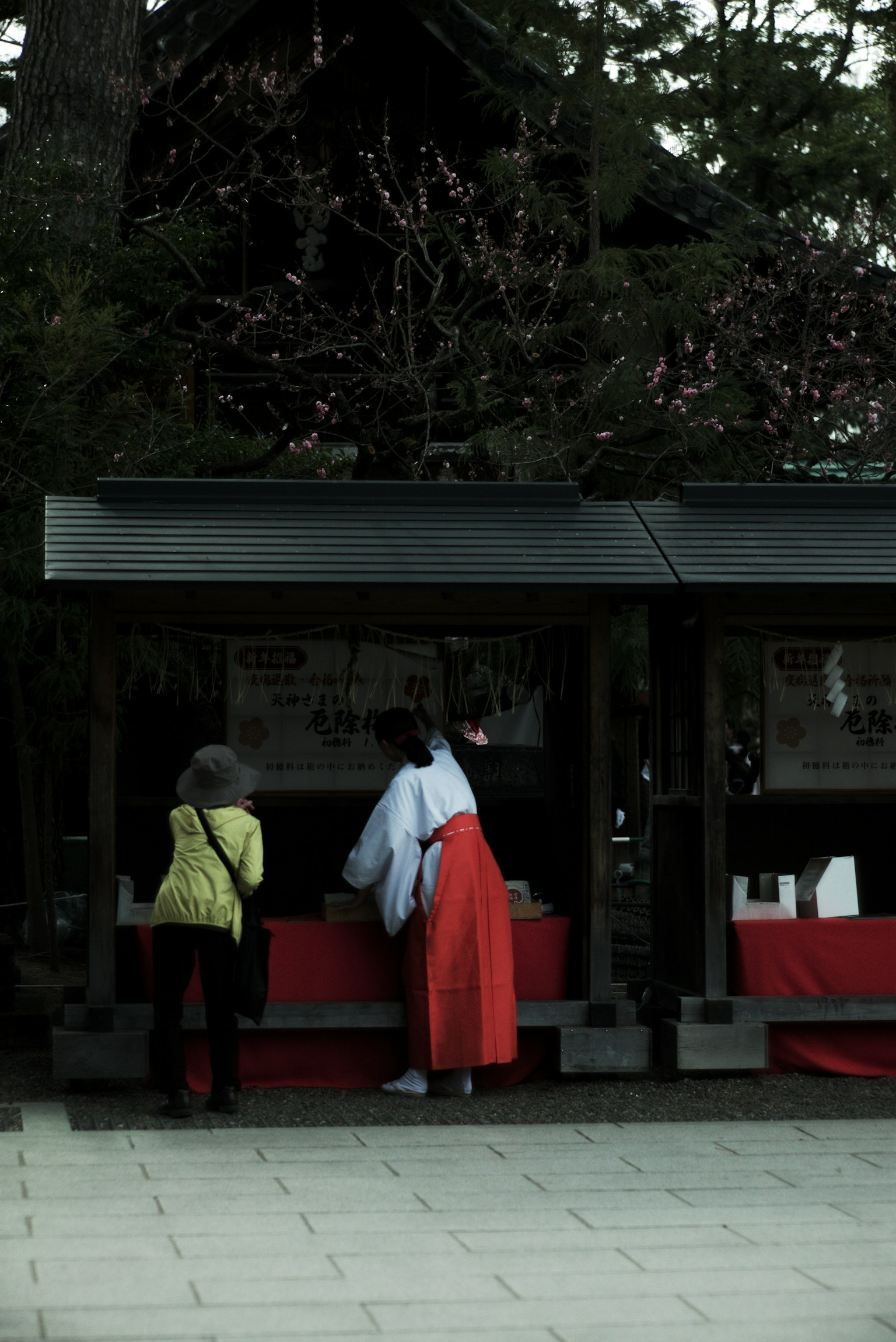 Scene at a shrine featuring a woman in red attire and another in yellow clothing