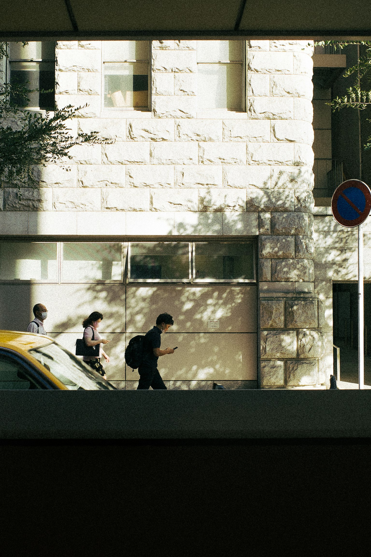 Menschen, die draußen neben einem Steingebäude mit Schatten gehen