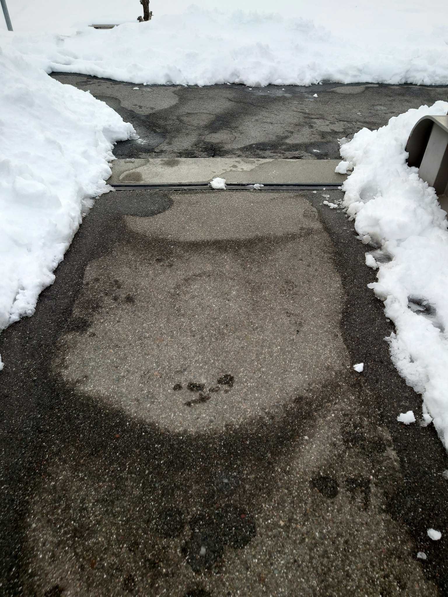 Nasse Asphaltfläche eines Gehwegs umgeben von Schnee