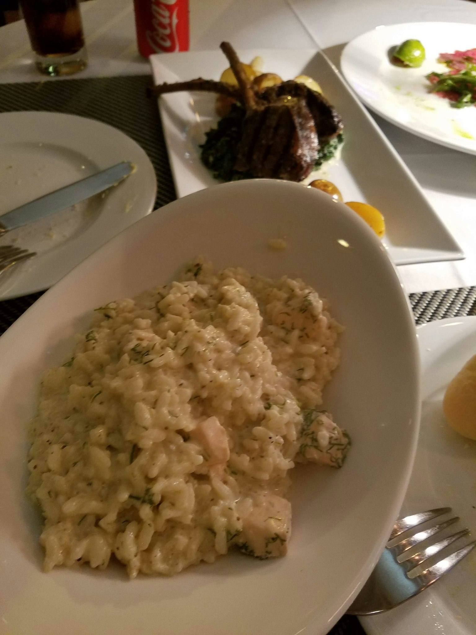 Risotto cremoso servido en un plato blanco con un plato a la parrilla al fondo