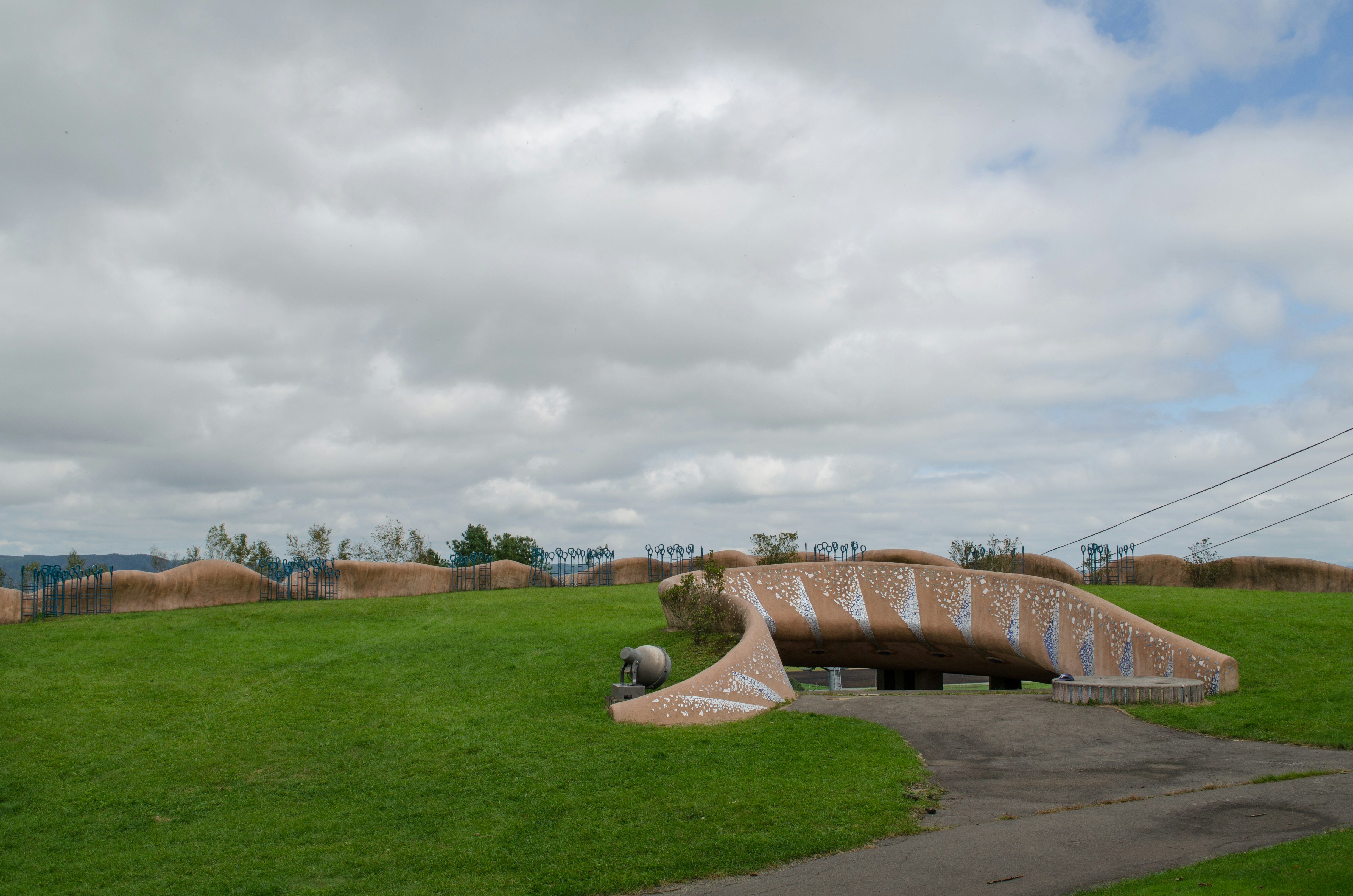 path through a park with grassy hills and a curved outdoor art installation