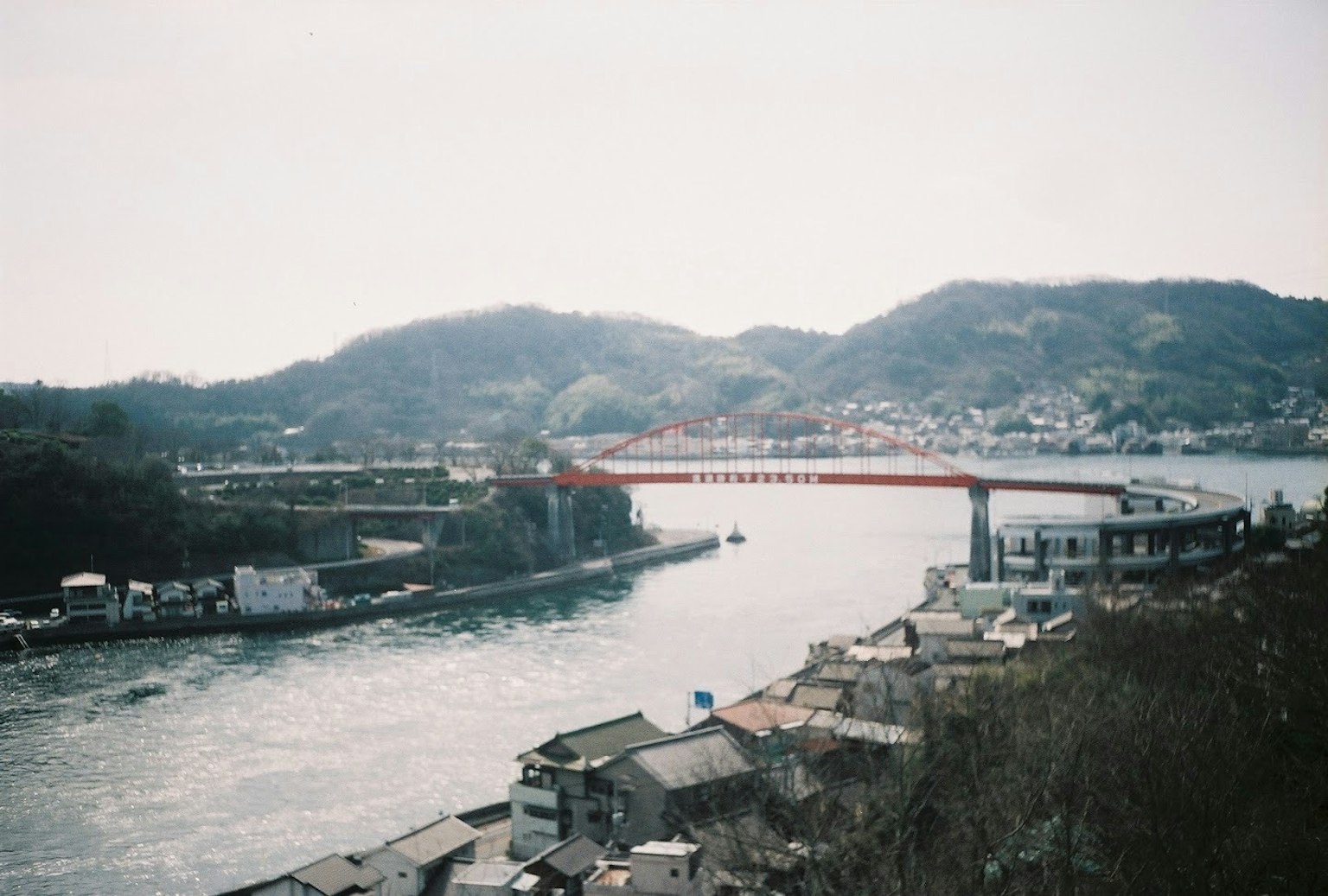 一座橫跨河流的紅色橋樑，背景是山丘