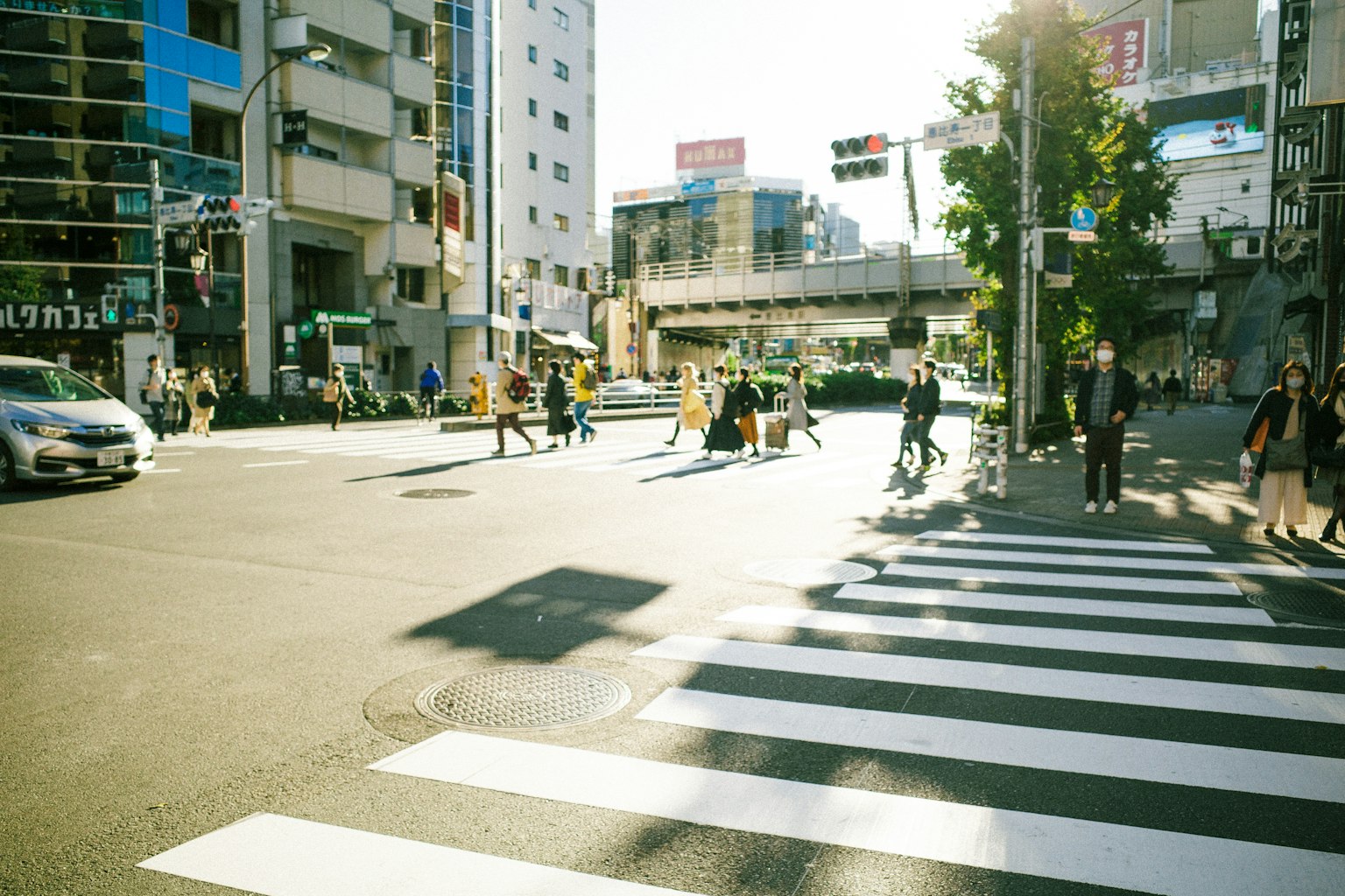 Scena urbana con pedoni e auto a un attraversamento pedonale sotto una luce solare brillante