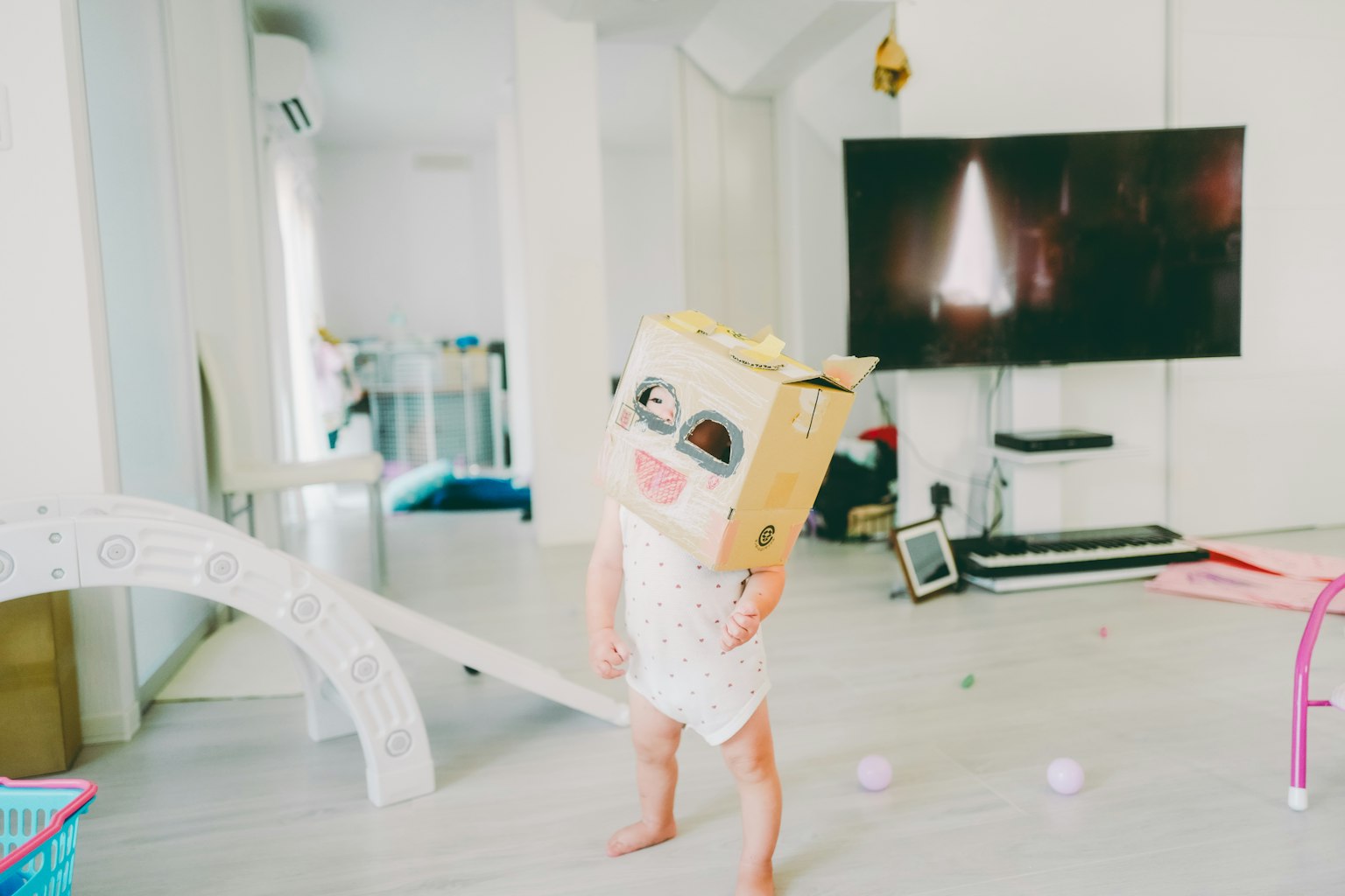 子供が段ボールの箱をかぶって笑顔で遊んでいる室内の風景