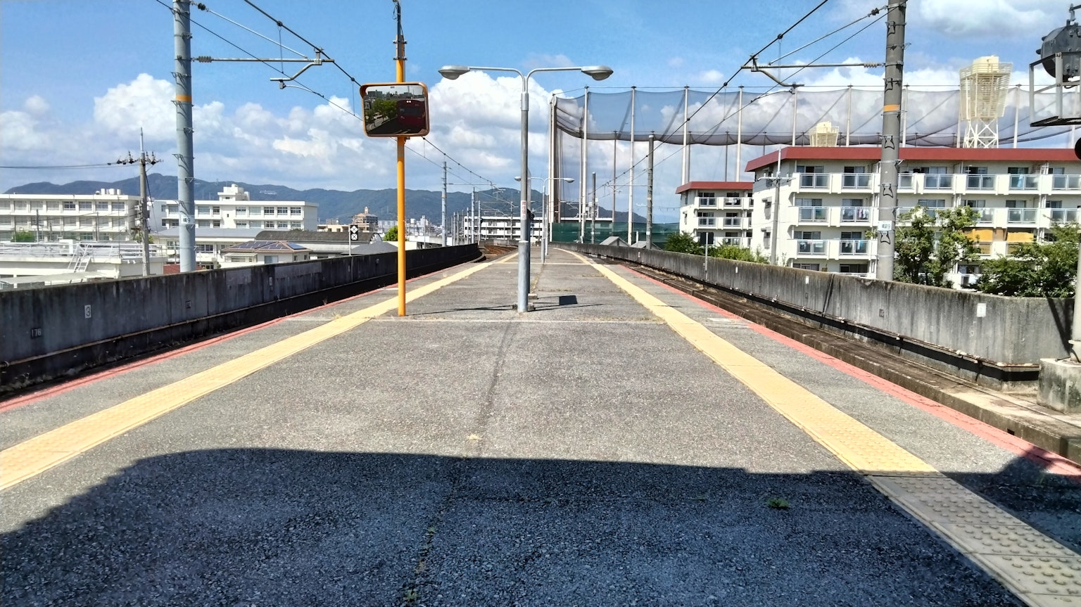Vue d'une plateforme de gare avec un ciel bleu et des nuages blancs entourant des bâtiments résidentiels