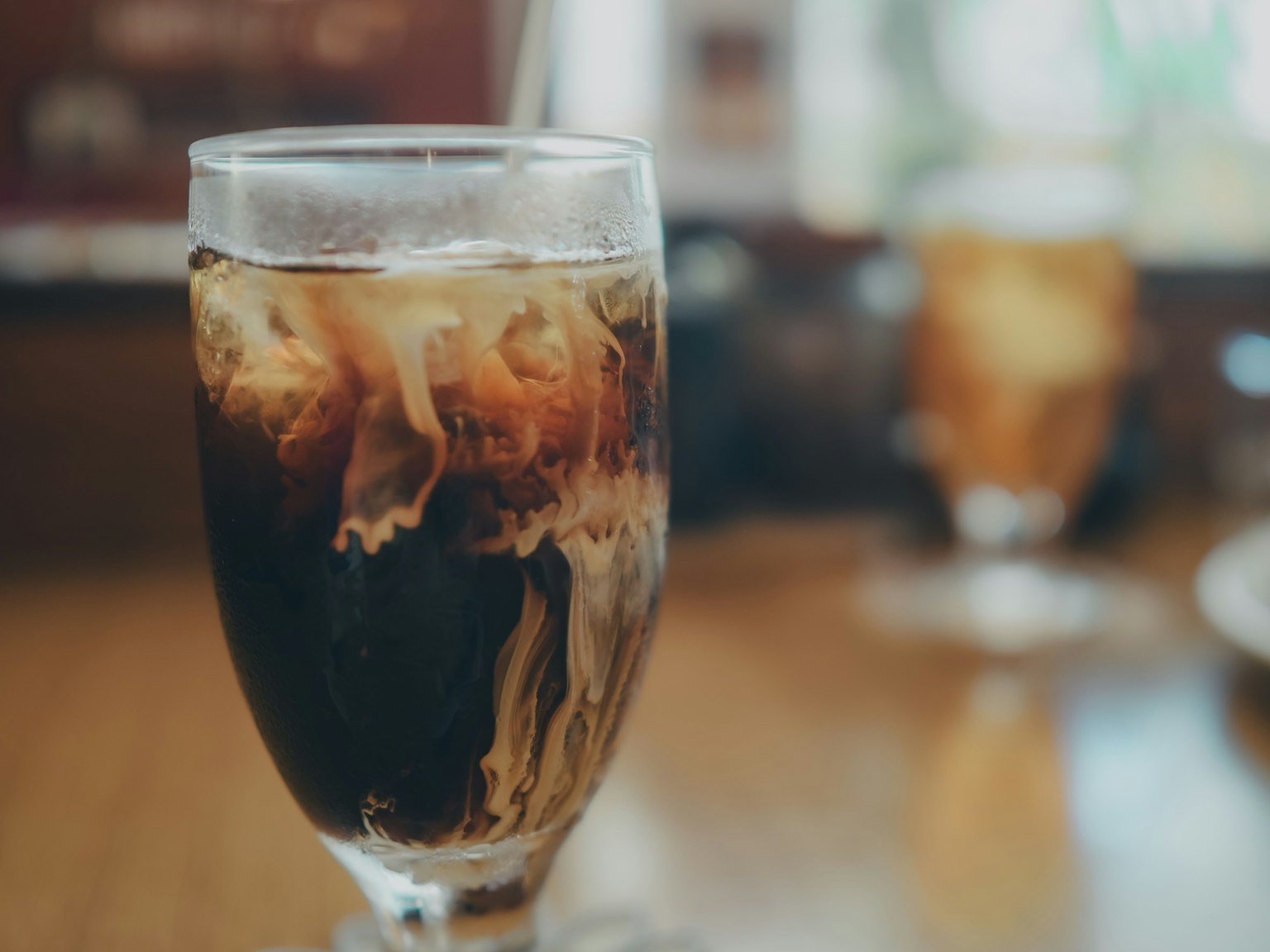A glass of iced coffee with swirling cream and a blurred background