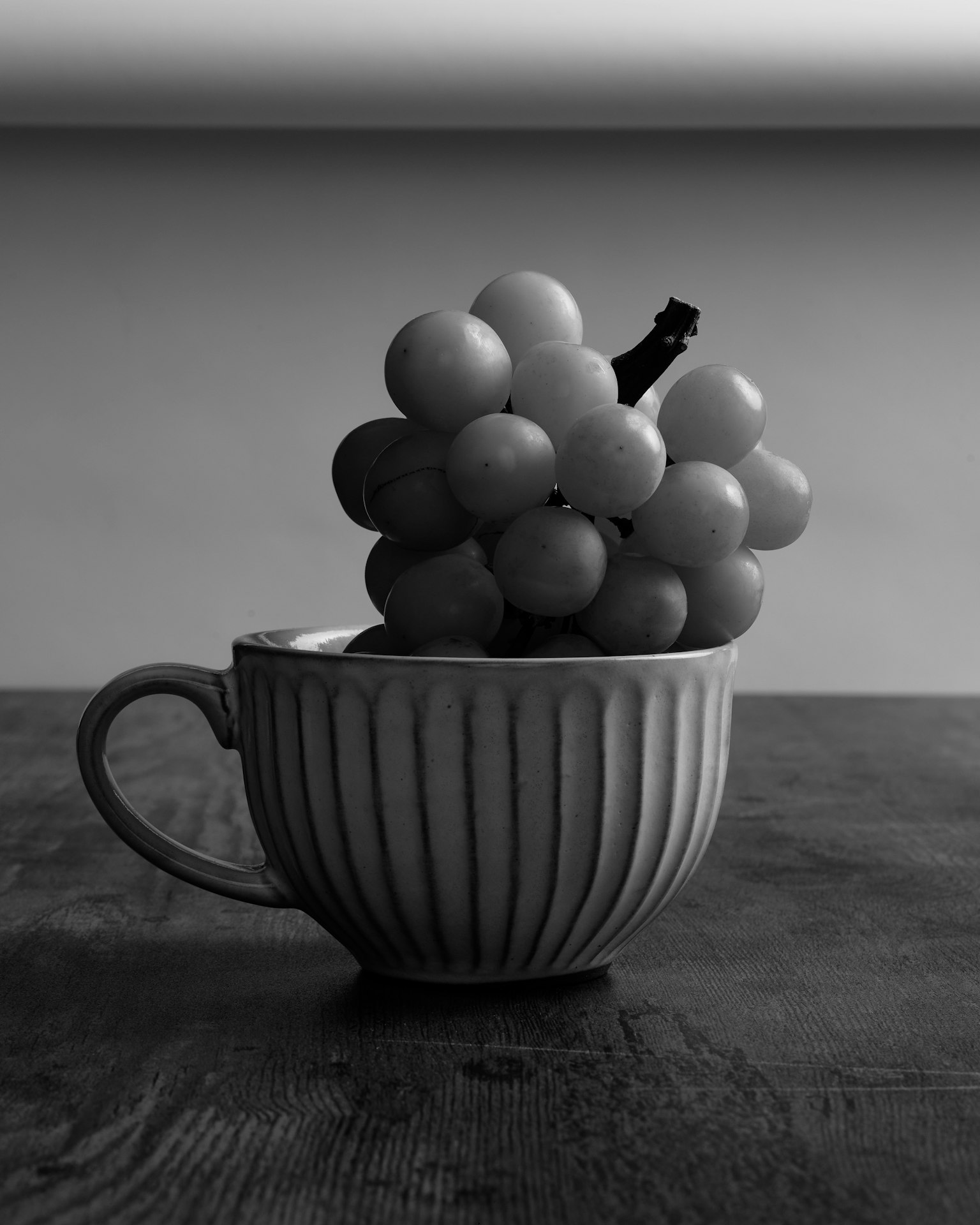 Un racimo de uvas en una taza a rayas contra un fondo degradado en blanco y negro