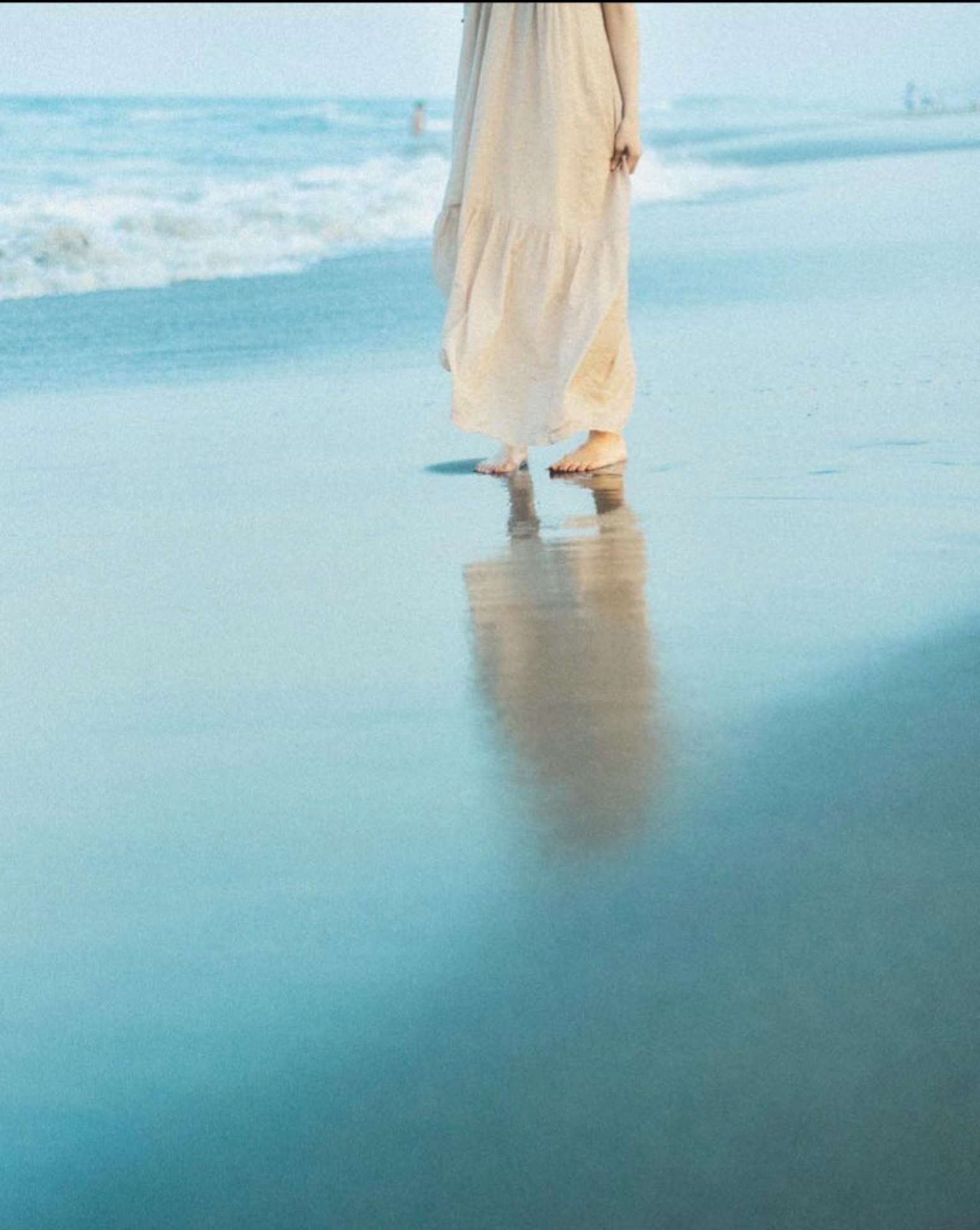ผู้หญิงในชุดสีขาวเดินอยู่บนชายหาด