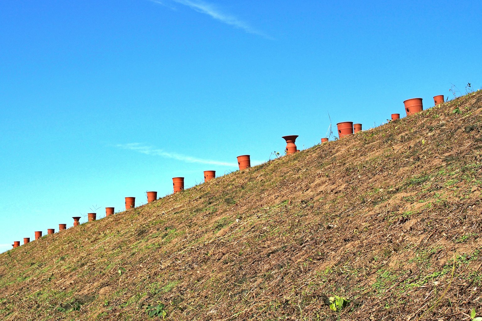 Ceramic pots arranged on a sloped hill under a blue sky