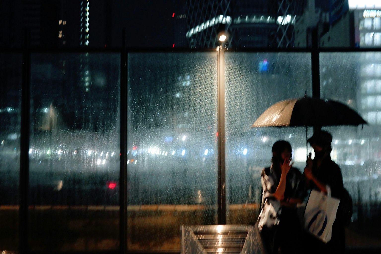 Two people holding an umbrella in the rain at night in a city with blurred lights in the background