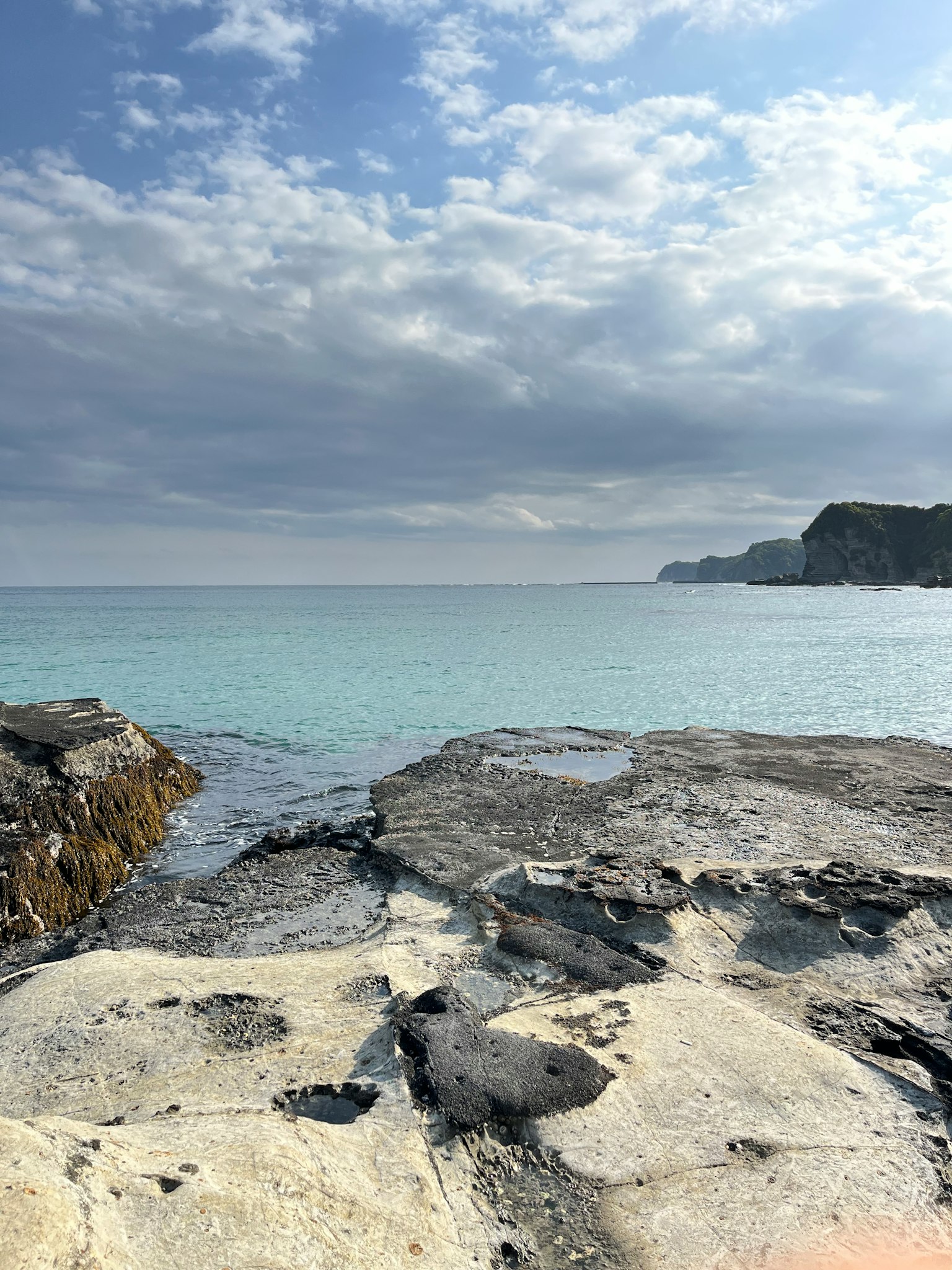 Mer bleue et côte rocheuse avec ciel lumineux et nuages