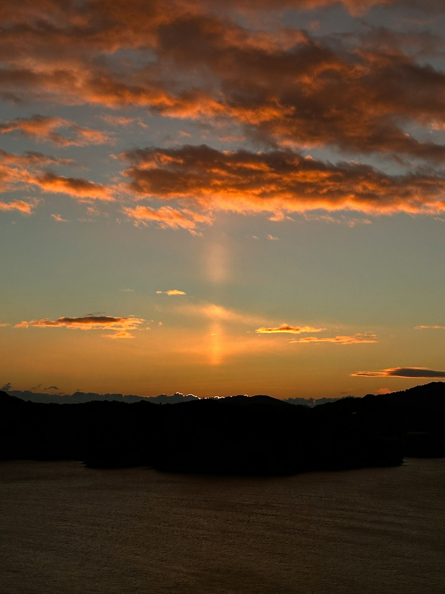 Bella paesaggio al tramonto con sfumature arancioni e blu, silhouette delle montagne, raggio di luce nel cielo