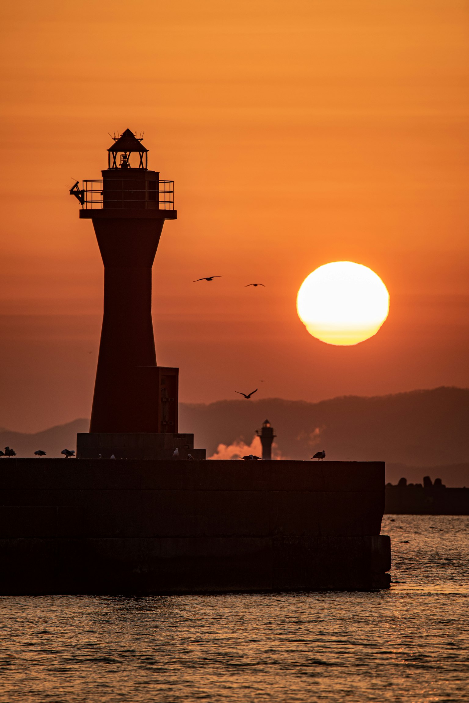 Silueta de un faro contra un atardecer en el océano