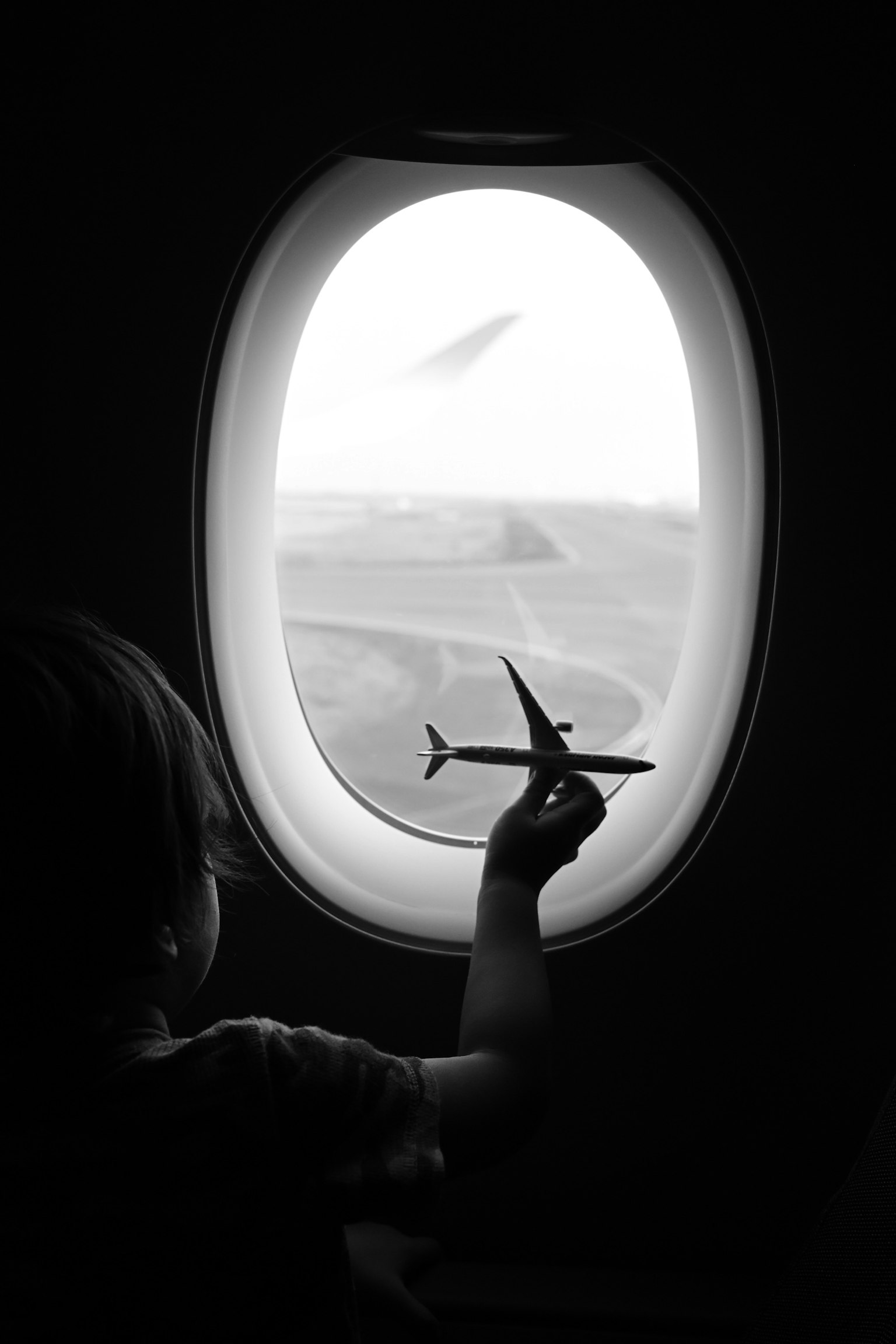 Child holding a toy airplane while looking out the airplane window