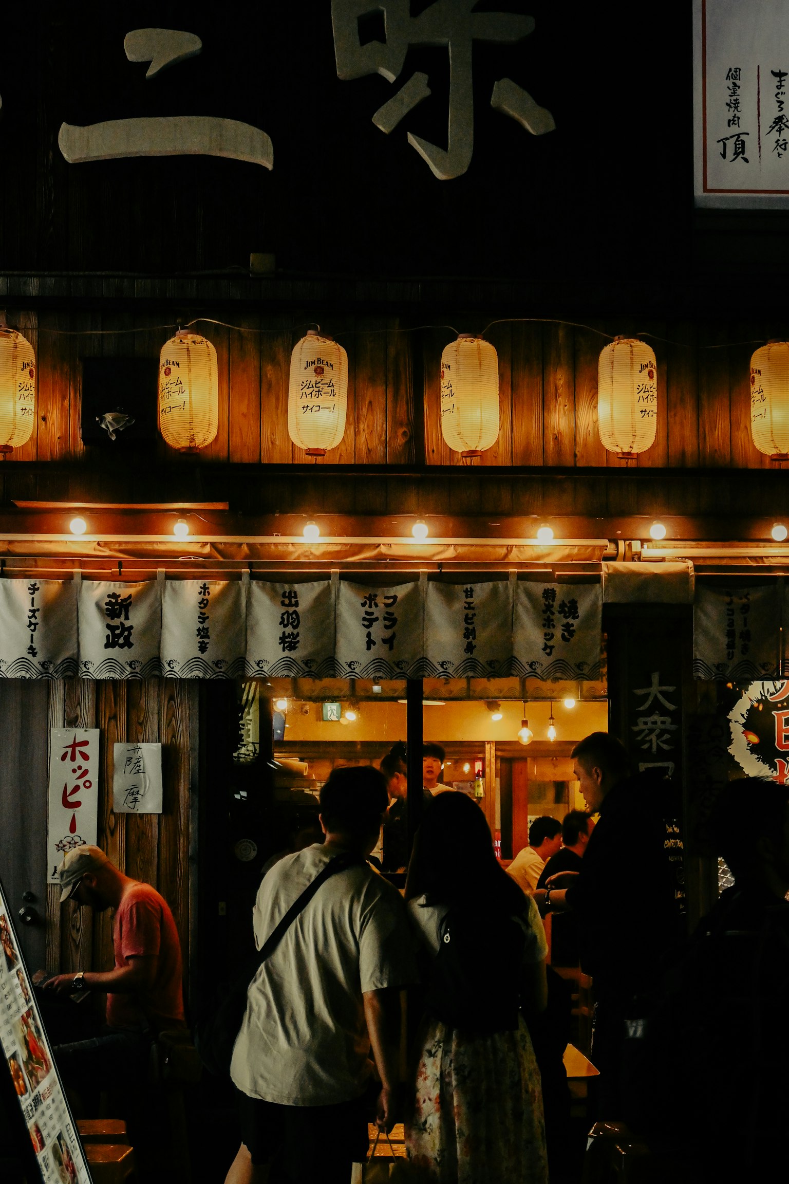 Exterior de un izakaya japonés por la noche con personas reunidas