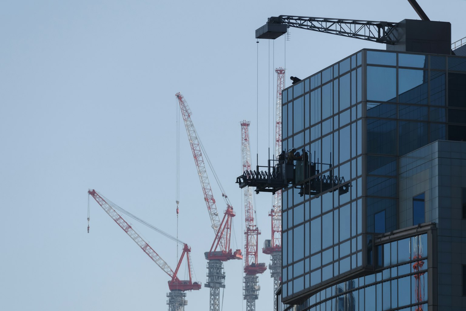 Pekerja membersihkan jendela gedung pencakar langit dengan crane di latar belakang