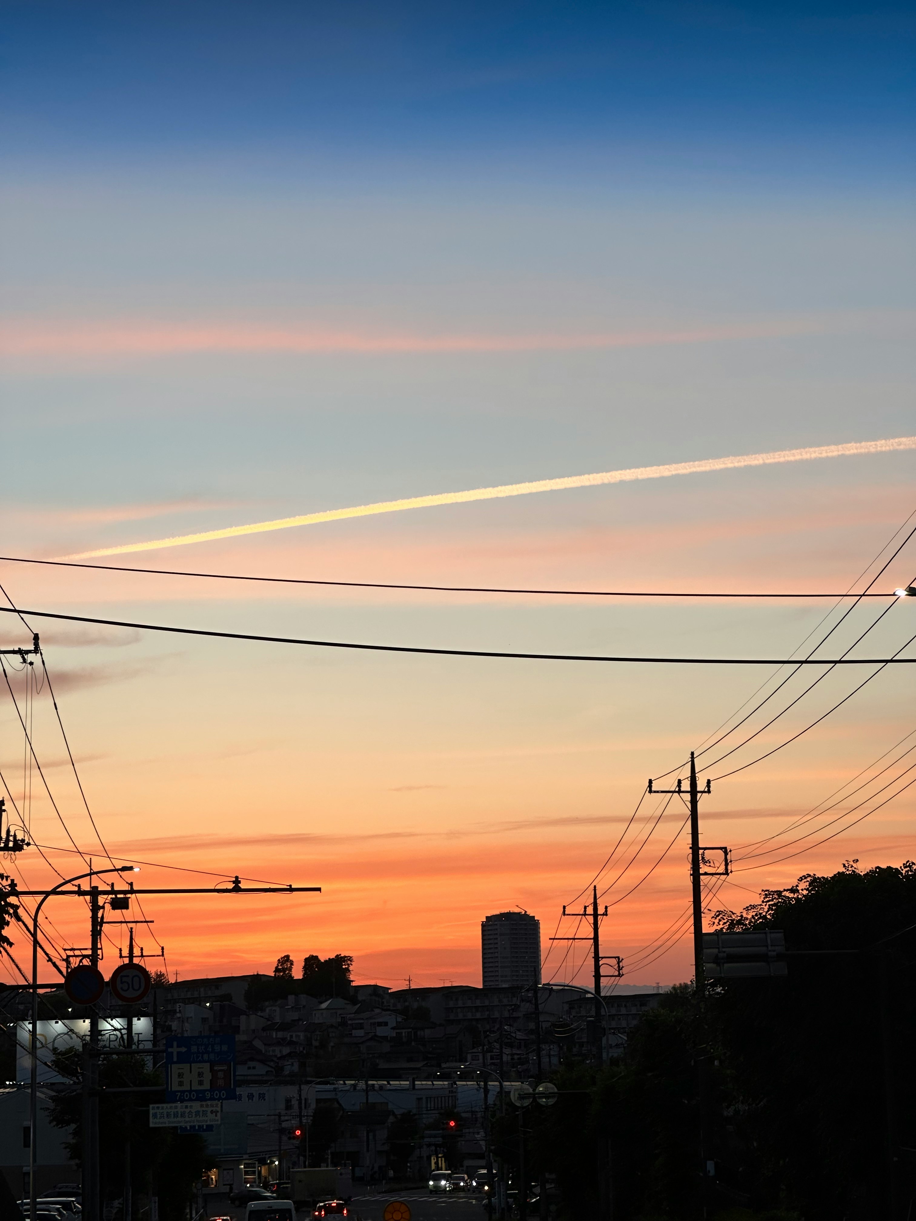 夕焼け空に飛行機雲が伸びる街の電線と屋根