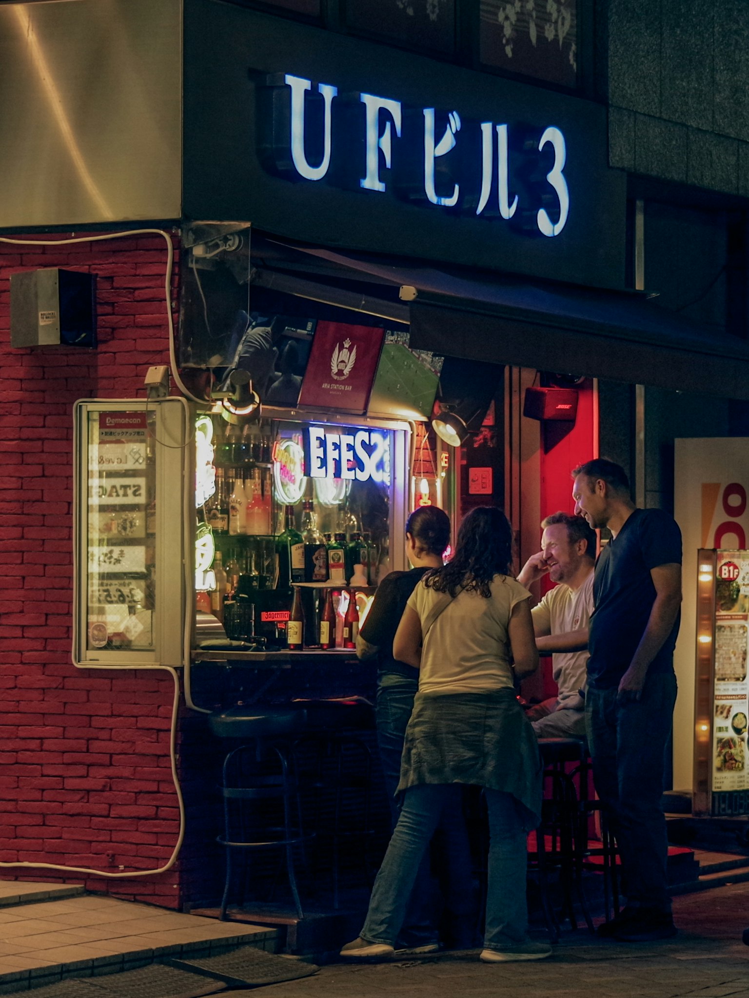 Mọi người trò chuyện bên ngoài quán bar với biển hiệu neon vào ban đêm