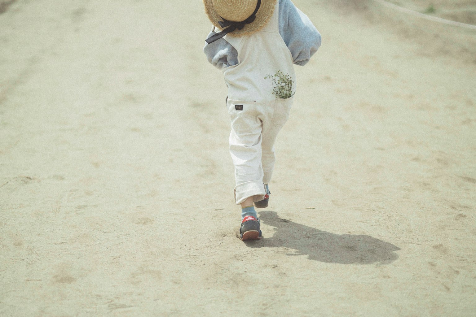 Bambino con cappello e pantaloni bianchi che cammina su un sentiero sabbioso