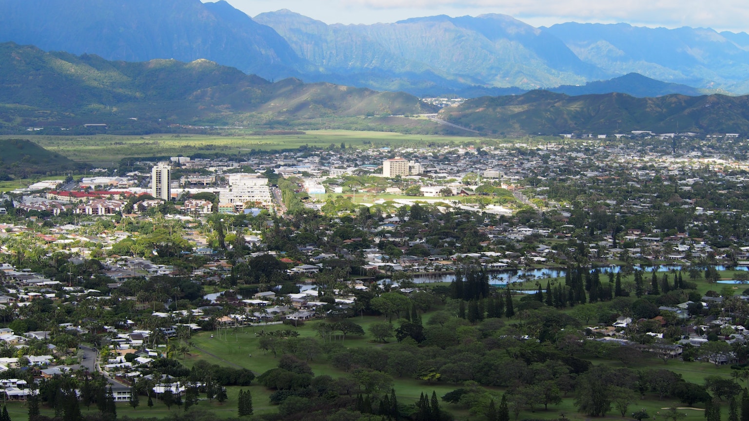 Un vaste paysage urbain entouré de montagnes avec des terrains verts et des bâtiments