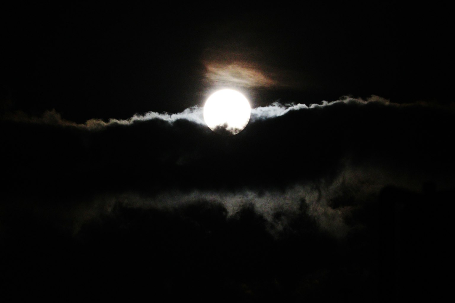 The moon peeking through clouds in a dark night sky