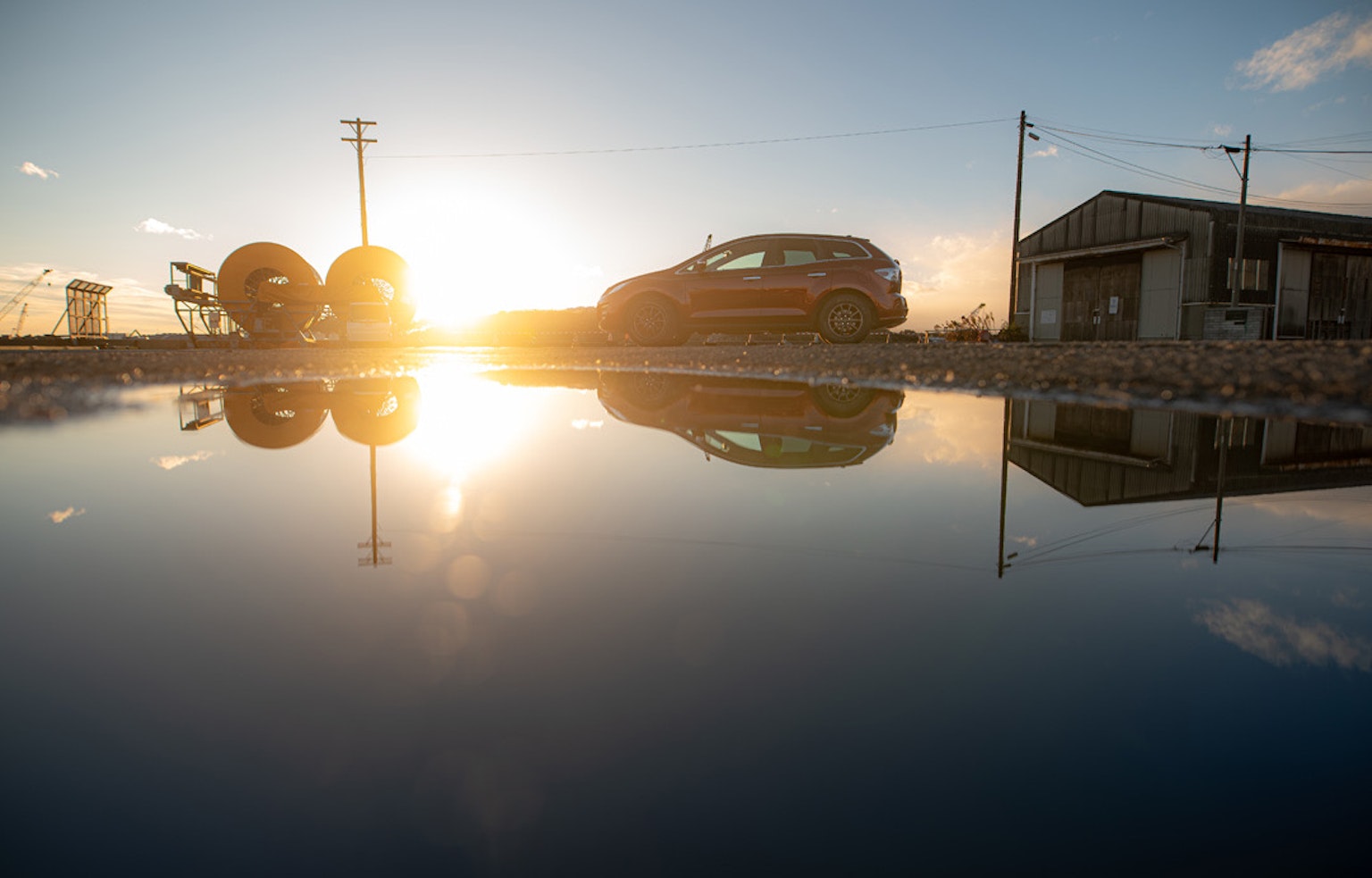 Reflejo del atardecer en un charco con un coche y un edificio