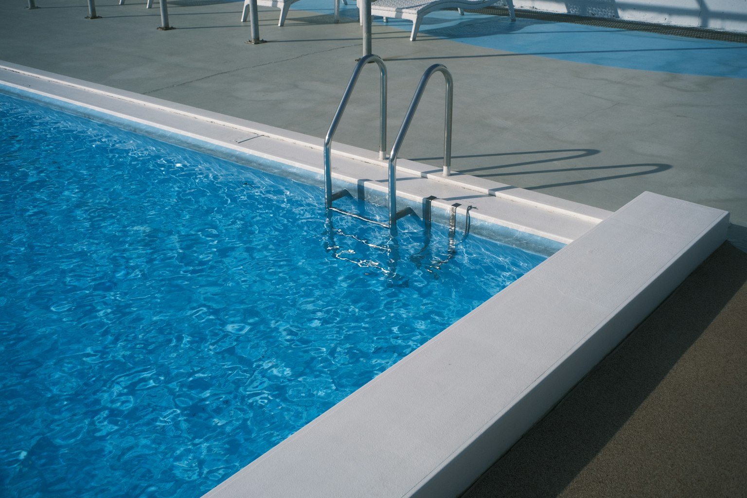 View of a blue swimming pool with metal steps at the side