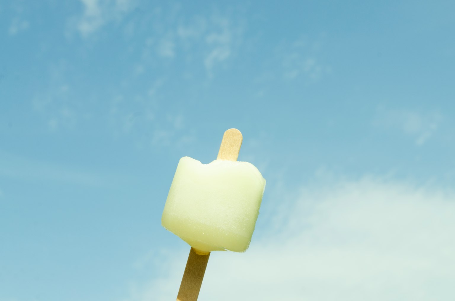 White ice pop on a stick against a blue sky