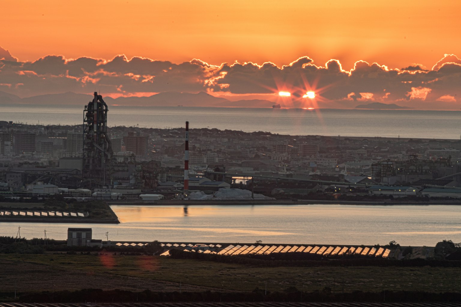Sonnenuntergang über dem Meer mit einem Leuchtturm und einem Hafen