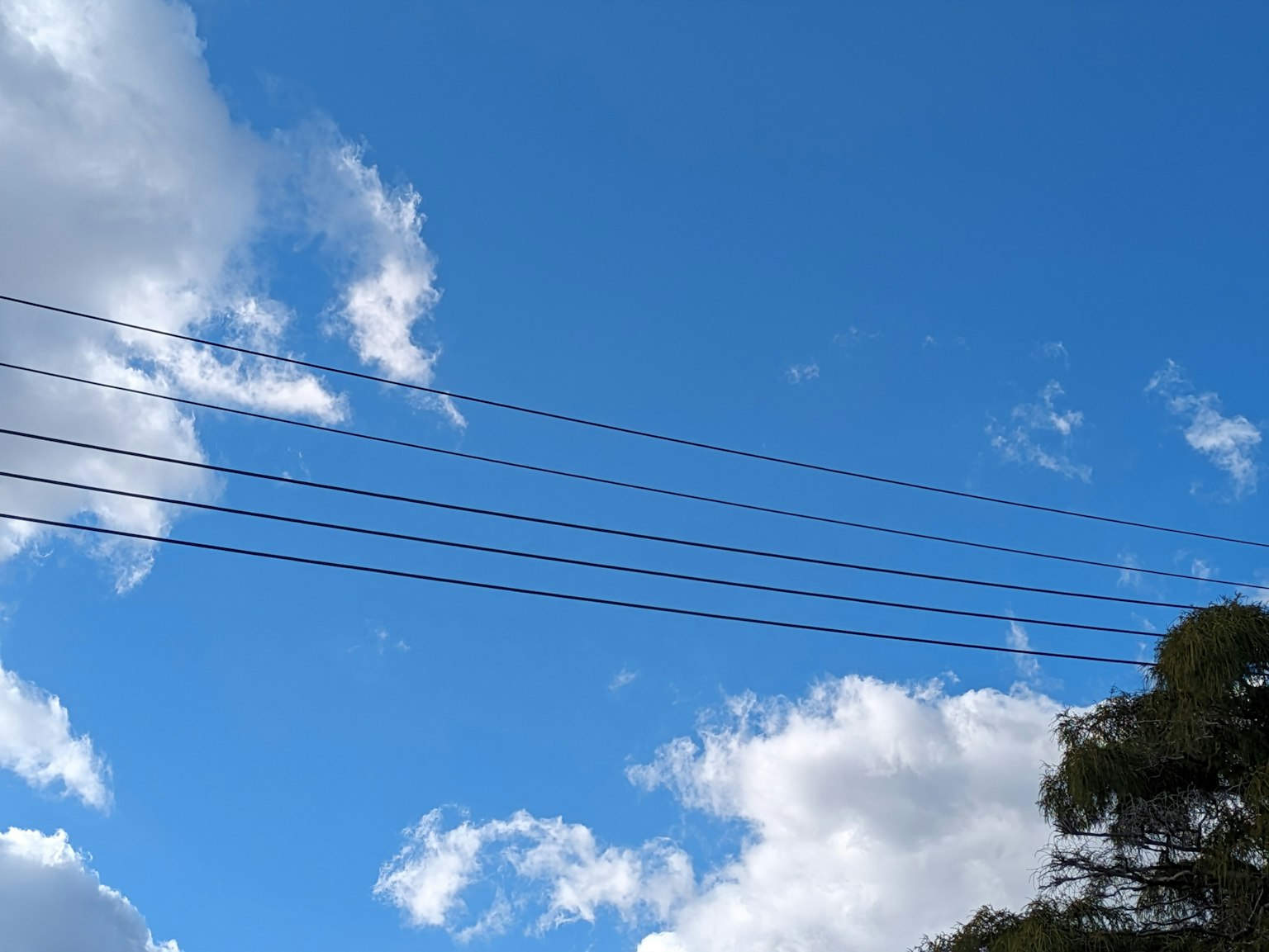 Stromleitungen vor einem hellblauen Himmel mit weißen Wolken